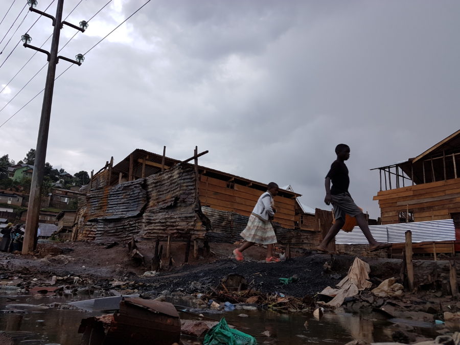 Two figures walk by houses and rubbish