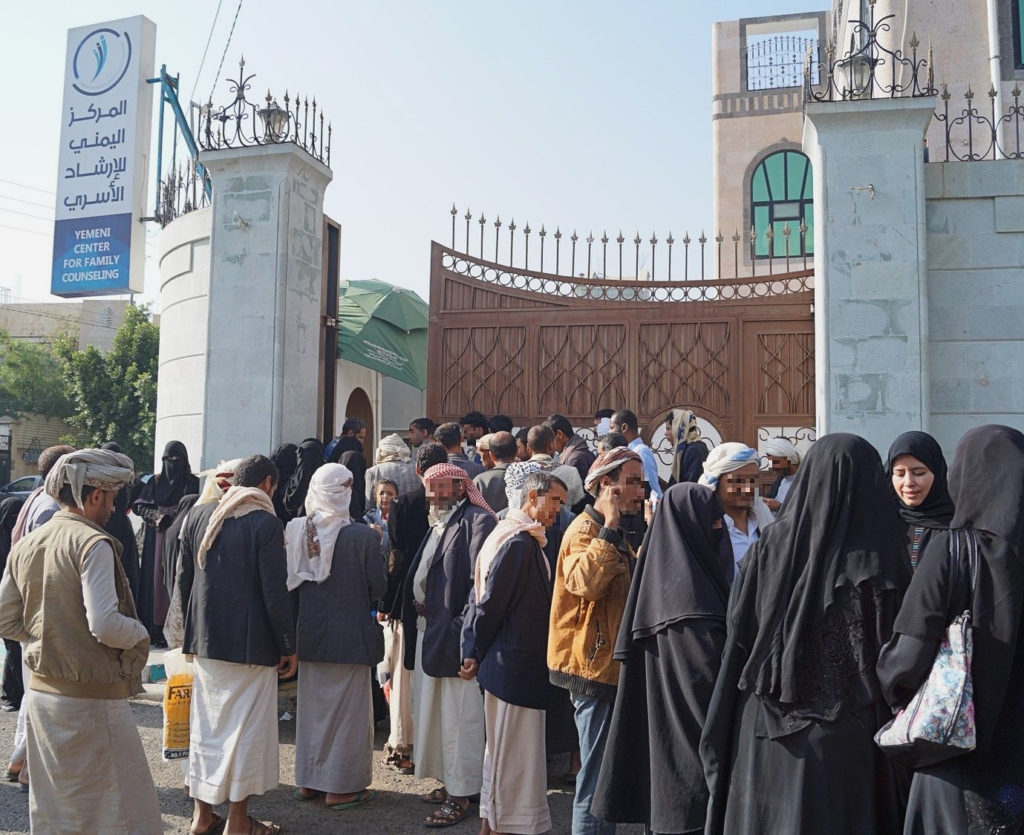 men and women queuing and waiting at a gate and wall