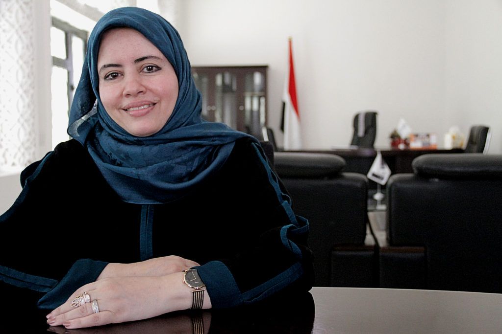 women looking into camera with a smile and hands on her desk