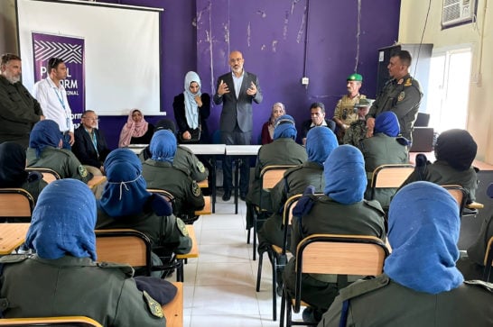 man in classroom stands in front of seated women in uniform