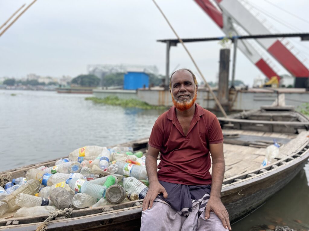 man sitting nest to a flat river boat filled with empty plastic bottles