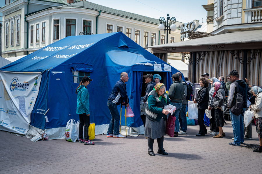 a big blue tent on a city square with people receiving aid and relief items