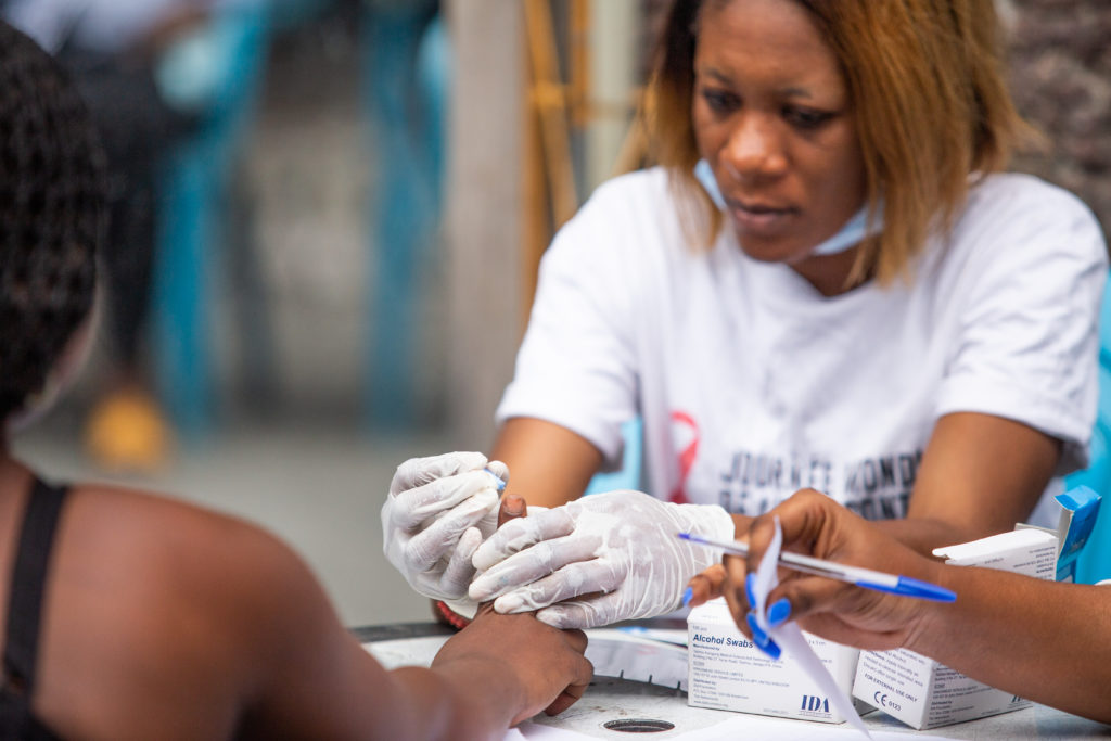 someone in a white shirt carrying medical gloves takes a finger blood test