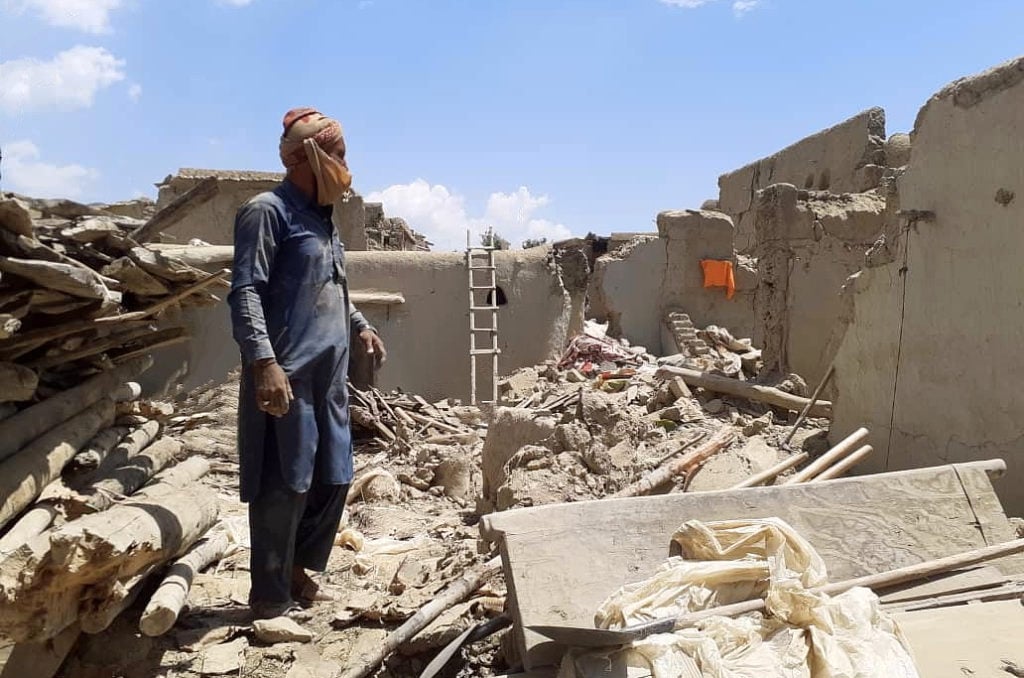 man standing on rubble of a collapsed house, under an open sky