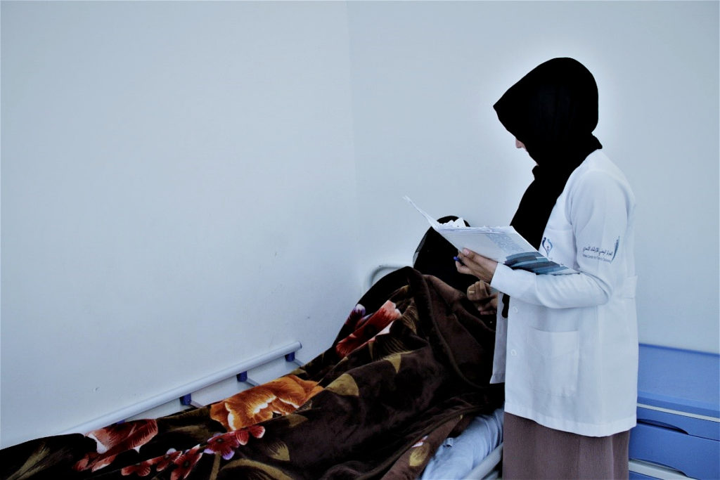 health worker standing next to a bed with a woman in a ward