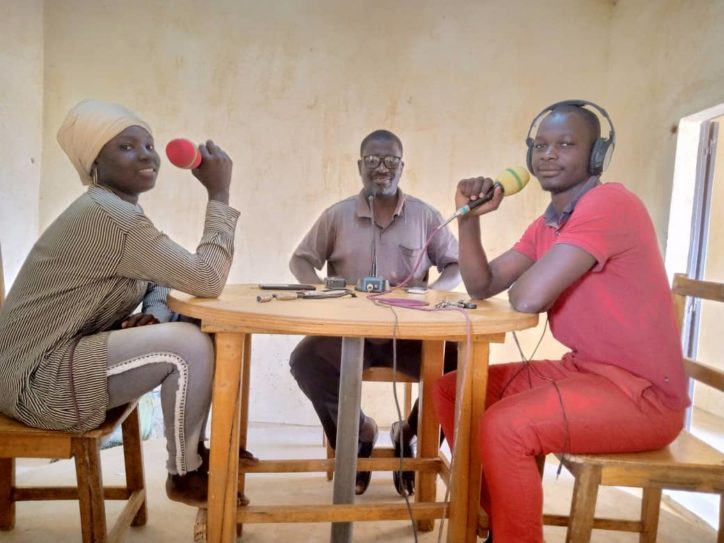 two young men one young woman sitting around a table in what looks like a radio studio