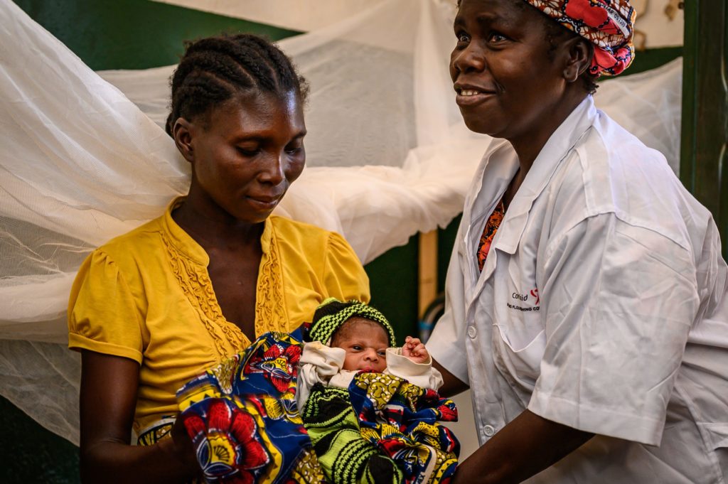 young mother with newborn child in her arms and midwife to her left also holding the baby