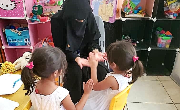 veiled woman clapping hands with two young girls in a room