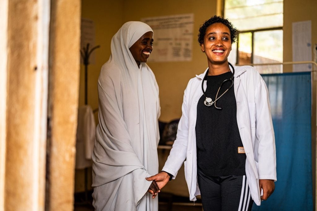 female doctor standing a doorway of a health faciltiy holding the hand of a female patient