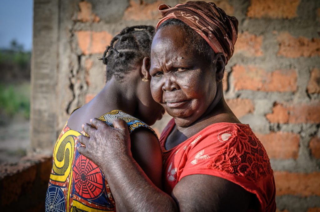 old lady looking into the camera and holding a young woman whose face you can't see in her arms