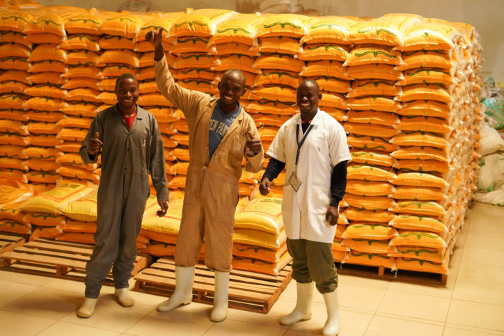 three men standing in a storage room full of rice sacks