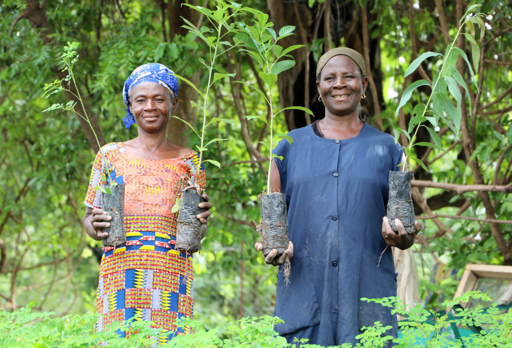 two women standing in lush green setting showing seedlings