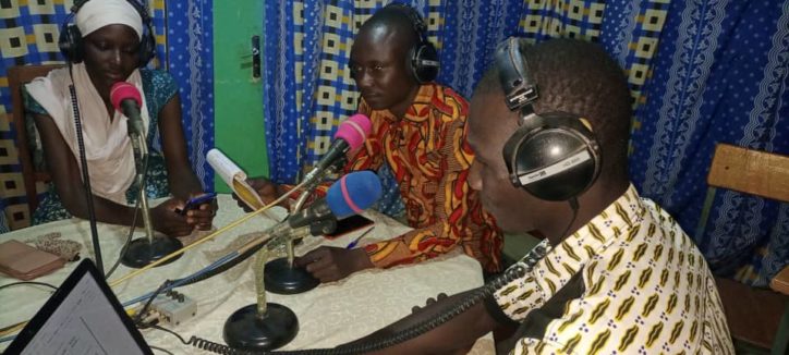 three youngsters around a table with headphones and microphones