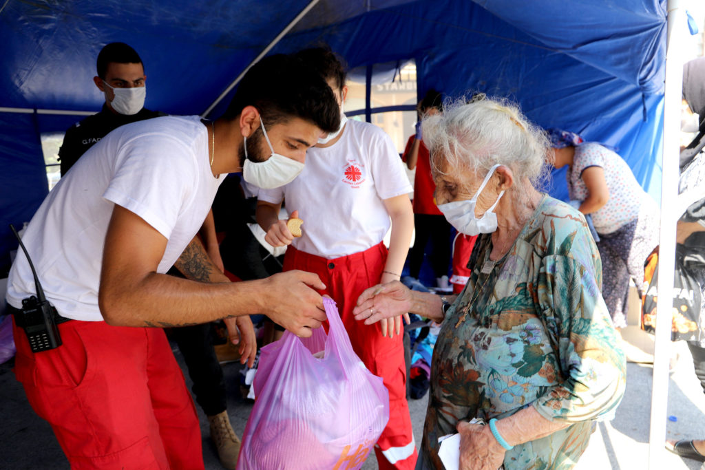 humanitarian relief site aid workers hand out bags to an old lady wearing face masks