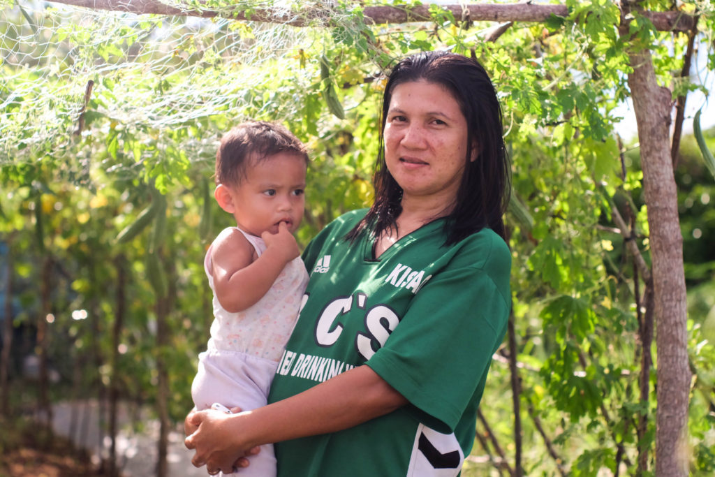 young woman holding a child standing in a vegetable garden