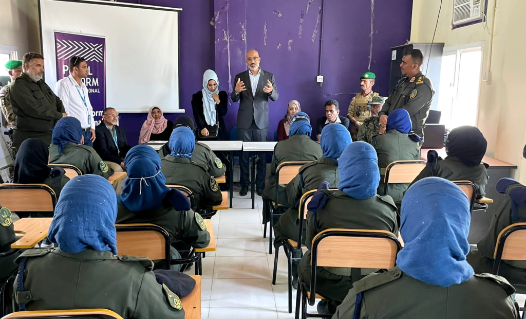 man in classroom stands in front of seated women in uniform