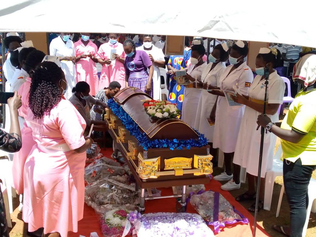 funeral scene with closed coffin surrounded by mourning people most of them dressed in medical staff outfits