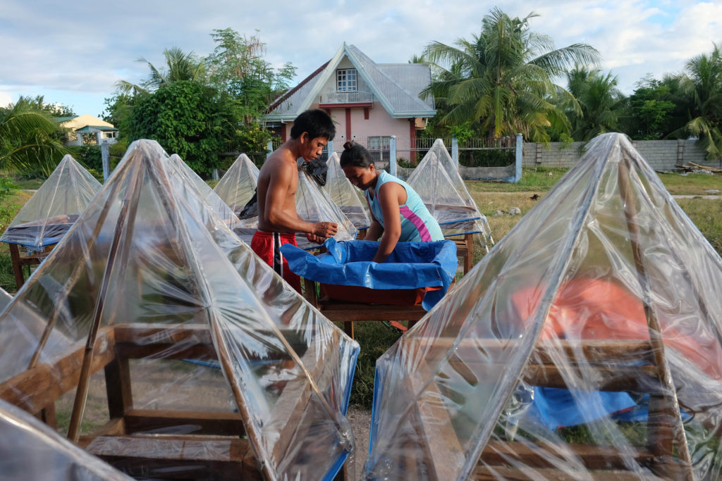 young man and young woman with wooden box and blue plastic sheet surrounded by a lot of desalinators made of wood and plastic foil