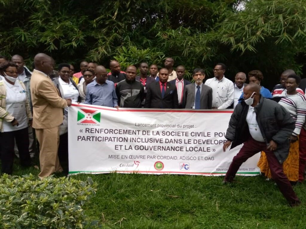 a group of some 30 people in a green garden setting holding a banner