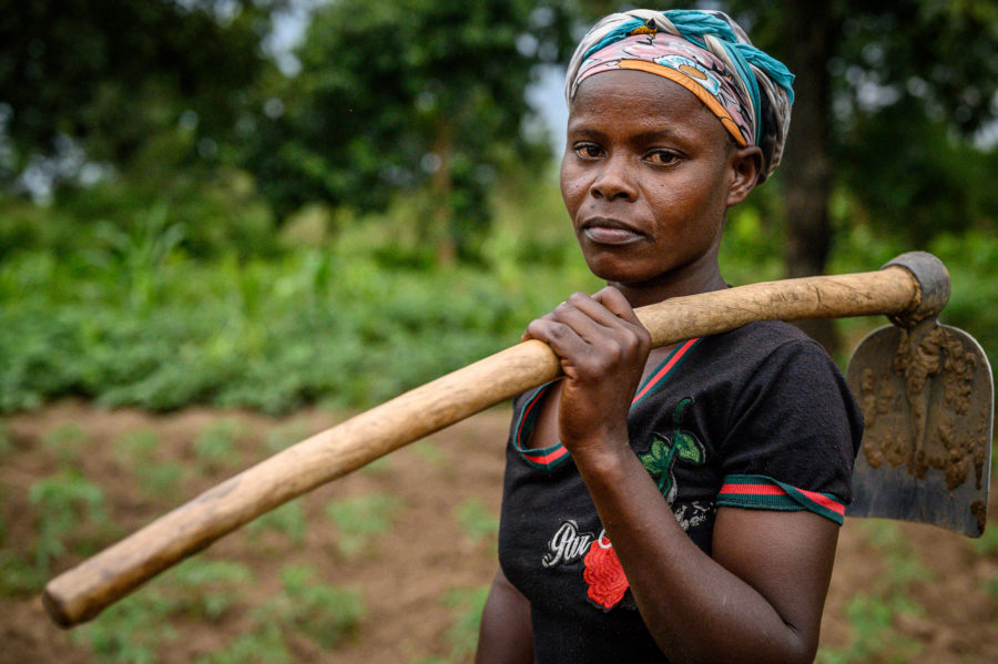 woman with hoe over her shoulder standing on farm plot