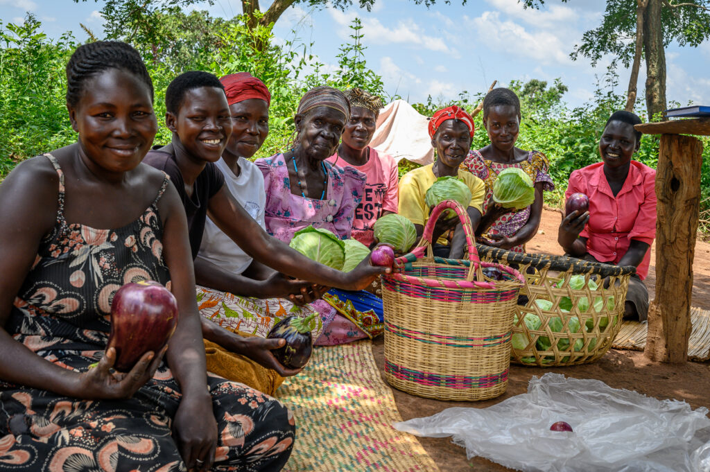 eight women sitting on the ground holding cabbages and other vegetables